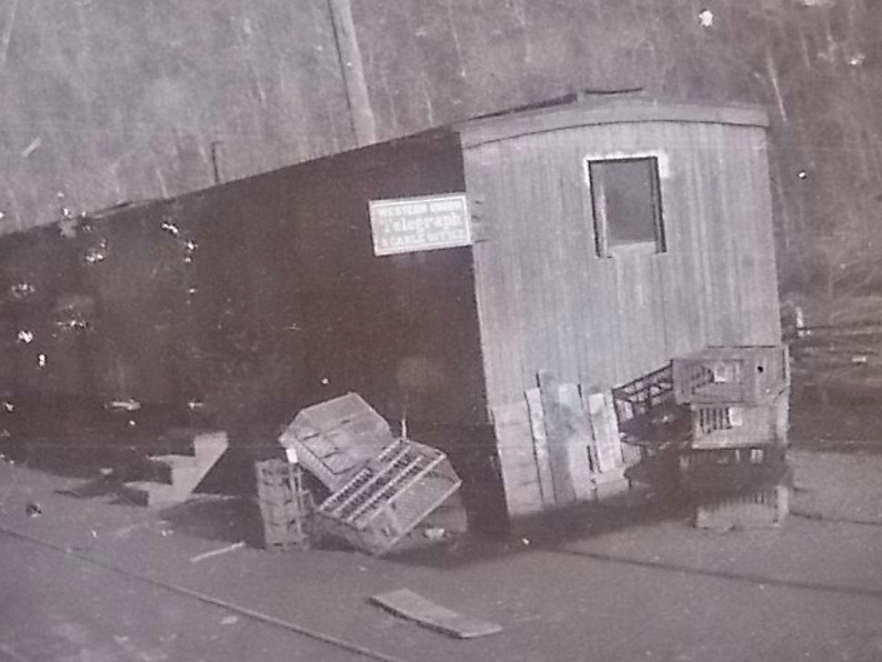 K&ouml;nnte beinhalten: Ein Schwarz-Wei&szlig;-Foto eines rechteckigen Geb&auml;udes mit der Aufschrift Western Union Telegraph & Cable Office. Das Bauwerk verf&uuml;gt &uuml;ber ein einzelnes Fenster, eine Treppe und mehrere Holzkisten, die an der Au&szlig;enwand gestapelt sind.