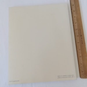 Pode incluir: Uma folha de papel retangular creme com texto no canto inferior direito. Uma r&eacute;gua de madeira com marca&ccedil;&otilde;es em polegadas &eacute; posicionada verticalmente ao longo da borda direita do papel.