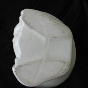 May include: A white ceramic object with a rounded base and a sculpted, textured surface. The object has a slightly aged appearance with some discoloration. The shape is irregular and appears to be a decorative item.