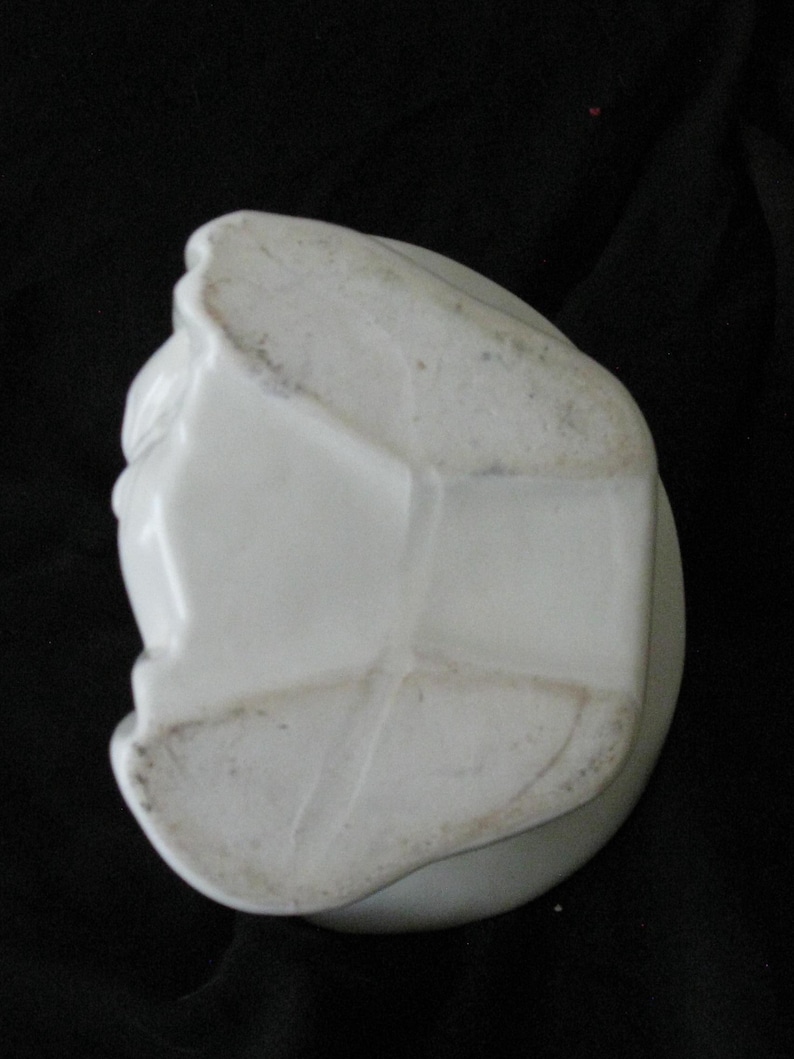 May include: A white ceramic object with a rounded base and a sculpted, textured surface. The object has a slightly aged appearance with some discoloration. The shape is irregular and appears to be a decorative item.