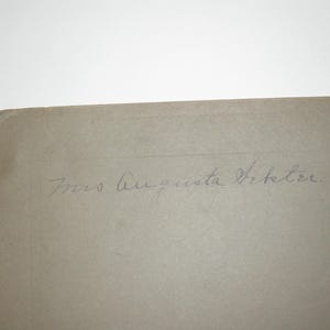 May include: A corner of a light tan, aged paper with the handwritten inscription "Mrs. Augusta Vetetre" in faded blue ink. The paper has a slightly rounded corner and appears to be an antique photograph or document.