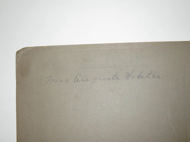 May include: A corner of a light tan, aged paper with the handwritten inscription "Mrs. Augusta Vetetre" in faded blue ink. The paper has a slightly rounded corner and appears to be an antique photograph or document.