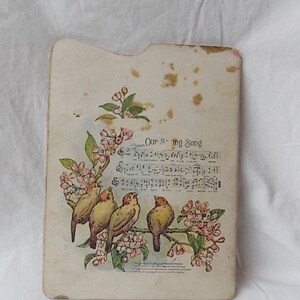 Puede incluir: Una tarjeta rectangular de color blanco roto con esquinas superiores redondeadas que presenta una ilustraci&oacute;n impresa de cuatro p&aacute;jaros posados en una rama florida. El dise&ntilde;o incluye notaci&oacute;n musical y el texto Our S-ing Song, con manchas.