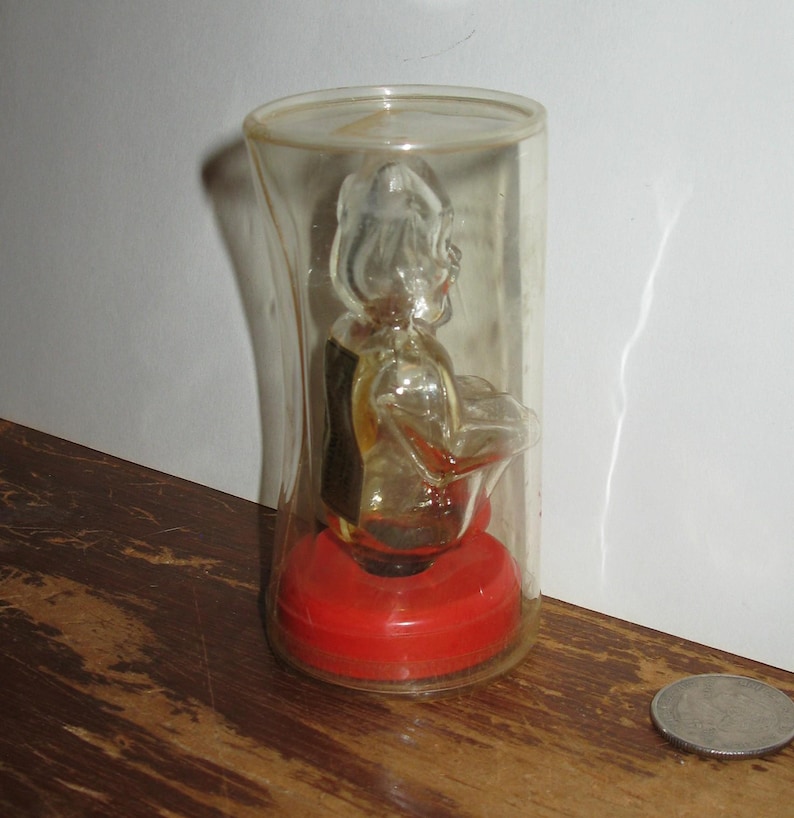 K&ouml;nnte beinhalten: Eine transparente Musikbox aus Kunststoff mit einer Figur im Inneren, die in einem zylindrischen Beh&auml;lter eingeschlossen ist. Die Figur spielt ein Musikinstrument. Der Sockel ist rot, und die Box steht auf einer Holzoberfl&auml;che.