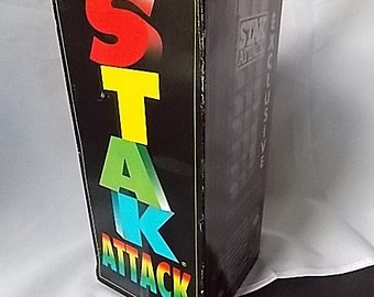 May include: A black rectangular game box for Stak Attack with the word STAK in large, colorful, stacked letters and the word ATTACK in a rainbow gradient. The side panel features the text Exclusive and a graphic of a stacked block tower.