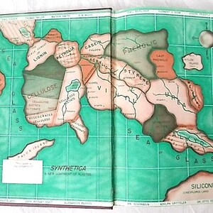 Peut inclure: Livre ouvert avec une illustration de carte intitul&eacute;e "Synthetica: Un nouveau continent de plastiques". La carte pr&eacute;sente des masses terrestres nomm&eacute;es Cellulose et Silicones, sur un fond quadrill&eacute; vert.