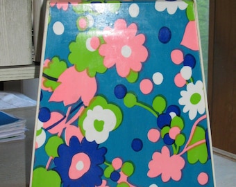 May include: A trapezoidal plastic carrying case with a white handle and a latch at the top. The front panel features a vibrant floral pattern on a blue background, displaying stylized flowers in shades of pink, lime green, white, and dark blue.