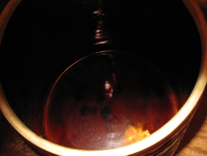 May include: A close-up shot of the interior of a brown ceramic crock. The interior is dark, with a glossy finish. The rim of the crock is a lighter brown color.