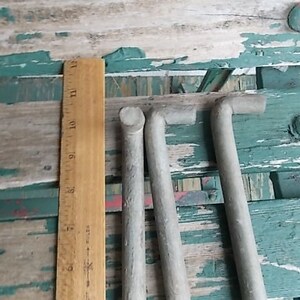May include: Three L-shaped metal rods with a matte gray finish, positioned vertically next to a wooden ruler. The ruler shows the rods measure approximately 12 inches in length. The rods have a cylindrical body and a bent top section.