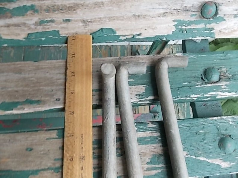 May include: Three L-shaped metal rods with a matte gray finish, positioned vertically next to a wooden ruler. The ruler shows the rods measure approximately 12 inches in length. The rods have a cylindrical body and a bent top section.
