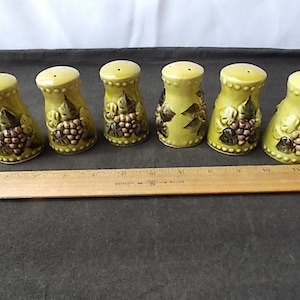 May include: Set of six ceramic salt and pepper shakers. The shakers are light green with a grape cluster design in brown and green. Each shaker has a small hole on top for dispensing and a rounded base.
