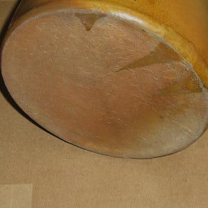 Pode incluir: Close-up da base de um pote de cer&acirc;mica marrom. O pote tem uma base arredondada e uma superf&iacute;cie texturizada. A cor &eacute; um marrom quente e terroso com algumas &aacute;reas mais claras.