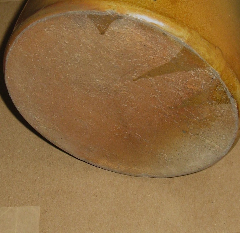 Pode incluir: Close-up da base de um pote de cer&acirc;mica marrom. O pote tem uma base arredondada e uma superf&iacute;cie texturizada. A cor &eacute; um marrom quente e terroso com algumas &aacute;reas mais claras.