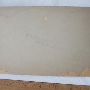 May include: A vintage photograph with a light tan background. The edges show signs of wear and discoloration. Faint text is visible, reading "Mr. & Mrs. C. Rigby, Jacksonville, Fla.". A wooden ruler is at the bottom.