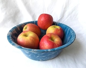 May include: A round, blue and white marbled enamel bowl containing five fresh red and yellow apples. The bowl features a swirling, cloud-like pattern across its exterior and interior surface, providing a contrast to the smooth, round fruit.