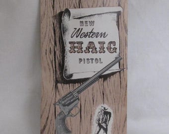 May include: A rectangular paper advertisement featuring a wood grain background with a scroll graphic displaying the text NEW Western HAIG PISTOL. A black and white illustration of a revolver is positioned diagonally across the center.