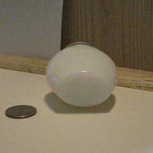 May include: A white, round, glass light fixture with a silver metal ring around the top. A coin is next to the light fixture. The light fixture is on a white surface.