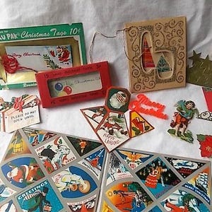 May include: A collection of vintage Christmas paper ephemera including a green Valu Pak of tags, a red box of cards, a gold glittered card, a die-cut angel, a red Merry Christmas sign, and two large sheets featuring various holiday illustrations.