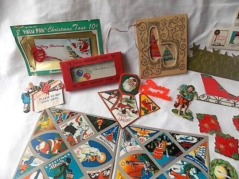 May include: A collection of vintage Christmas paper ephemera including a green Valu Pak of tags, a red box of cards, a gold glittered card, a die-cut angel, a red Merry Christmas sign, and two large sheets featuring various holiday illustrations.