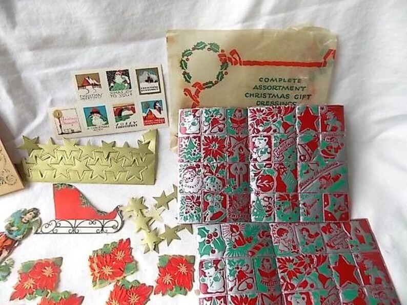 May include: A vintage Christmas gift dressing set including a printed paper envelope, a sheet of six holiday stickers, a gold star garland, a red and white sleigh cutout, and multiple sheets of red, green, and silver foil Christmas seals.