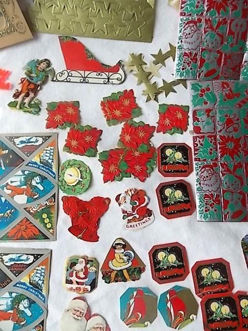 May include: A collection of vintage Christmas paper ephemera including die-cut poinsettias, Santa Claus figures, a red sleigh, gold foil stars, and rectangular gift tags with candle illustrations, all featuring festive red, green, and gold colours.