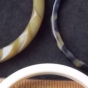 May include: Three vintage bangles in shades of green, black, and white. One bangle has a twisted design, while the others are smooth. The bangles are made of a glossy material and are likely from the mid-century era.