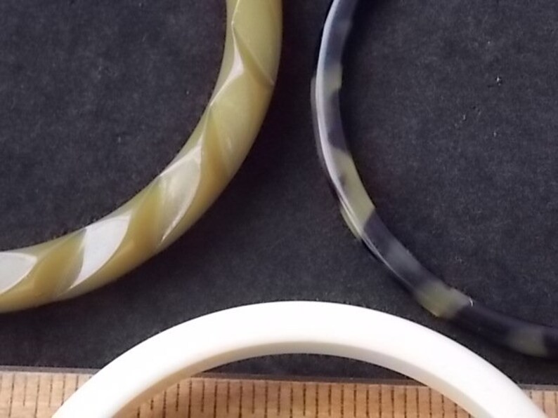 May include: Three vintage bangles in shades of green, black, and white. One bangle has a twisted design, while the others are smooth. The bangles are made of a glossy material and are likely from the mid-century era.