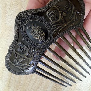 Op de afbeelding: Een vintage, sierlijke, bronzen haar kam met een bloemenmotief. De kam heeft een decoratieve, gegolfde rand en een rij tanden.