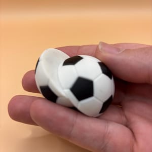 Könnte beinhalten: Ein schwarzer und weißer Fußball-Stressball aus weichem, quietschweichem Material. Der Ball ist leicht zusammengedrückt, wodurch das Innere des Spielzeugs sichtbar wird.