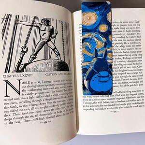 Puede incluir: Un marcap&aacute;ginas colorido con un Totoro azul sobre un cielo estrellado arremolinado, al estilo de Van Gogh. El marcap&aacute;ginas est&aacute; en un libro abierto con ilustraciones en blanco y negro.