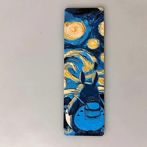 Puede incluir: Un marcap&aacute;ginas rectangular con una escena de noche estrellada al estilo de Van Gogh, con un personaje de dibujos animados en primer plano. El personaje es azul oscuro con una mochila azul claro.