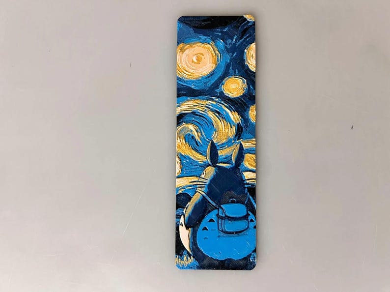 Puede incluir: Un marcap&aacute;ginas rectangular con una escena de noche estrellada al estilo de Van Gogh, con un personaje de dibujos animados en primer plano. El personaje es azul oscuro con una mochila azul claro.