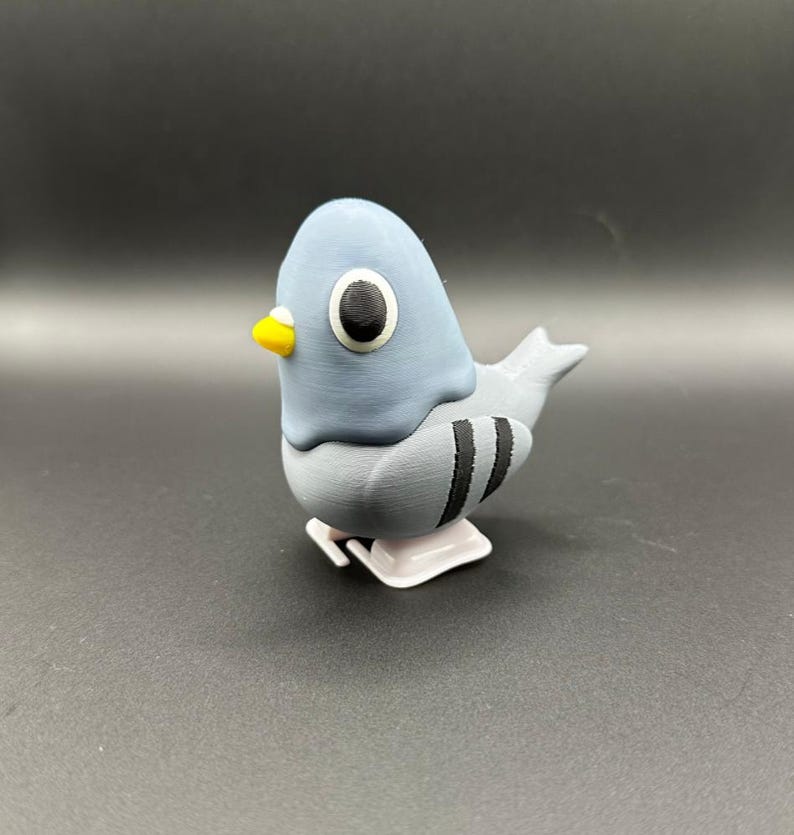 May include: A gray and white wind-up toy pigeon with black stripes. The toy has a yellow beak and large black eyes.