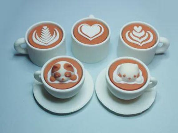 A tiny mechanical clicker toy disguised as a latte art coffee cup with mix-and-match interchangeable tops — the kind of satisfying desk fidget that every coffee person will immediately grab and never put down.