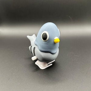 May include: A gray and white wind-up toy pigeon with black stripes on its tail. The toy has large black eyes and a yellow beak.