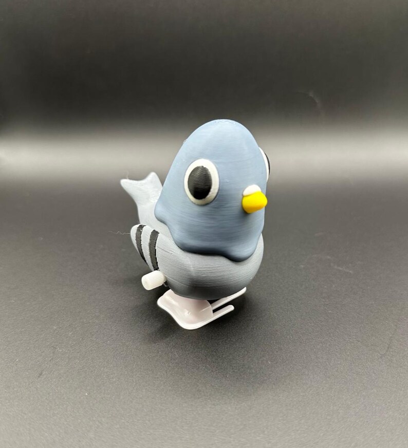 May include: A gray and white wind-up toy pigeon with black stripes on its tail. The toy has large black eyes and a yellow beak.