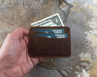 May include: A brown leather wallet with two American Express credit cards inside. The wallet has a simple design with a stitched edge.