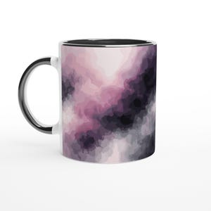 Könnte beinhalten: Weiße Keramiktasse mit schwarzem Henkel und Rand. Die Tasse hat ein Aquarelldesign in Rosa-, Lila- und Grautönen. Das Design bedeckt die gesamte Oberfläche und erzeugt einen einzigartigen Look. Eine stilvolle Ergänzung für jede Küche.