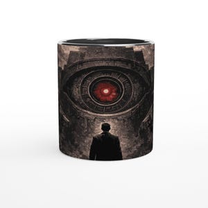 Peut inclure: Un mug cylindrique avec un design surréaliste. L'œuvre représente un grand œil menaçant avec un iris rouge, au-dessus d'une silhouette en manteau sombre. Le mug a un intérieur noir et un bord argenté.