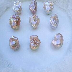 May include: Nine iridescent baroque pearls with a lustrous, pearlescent sheen. The pearls display a range of colours, including pink, gold, and white, and are arranged on a white, fluffy surface. The irregular shapes of the pearls add to their unique appeal.