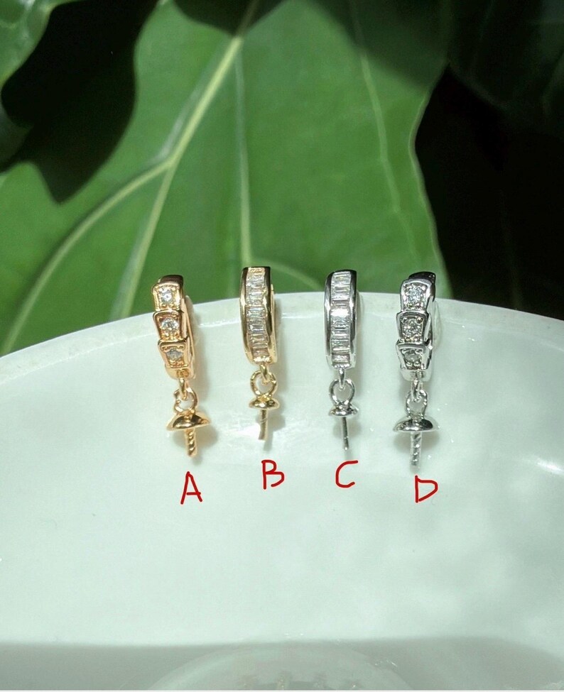 Puede incluir: Se muestran cuatro pares de pendientes en tonos dorados y plateados. Cada pendiente tiene un dise&ntilde;o de aro con piedras preciosas incrustadas. Los pendientes est&aacute;n etiquetados A, B, C y D. El fondo es una superficie blanca con follaje verde.