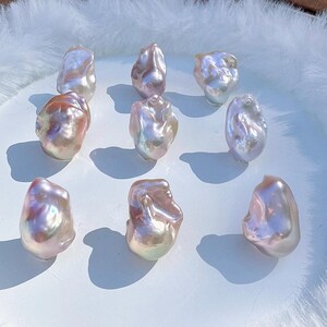 May include: Nine iridescent baroque pearls with a lustrous, pearlescent sheen. The pearls display a range of colours, including pink, peach, and white, and are irregularly shaped. They are arranged on a white surface.