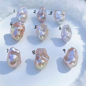 May include: Nine irregularly shaped, iridescent pearls are arranged on a white surface. The pearls display a range of colours, including pink, lavender, and gold, with a lustrous sheen. Each pearl is numbered from 1 to 9.
