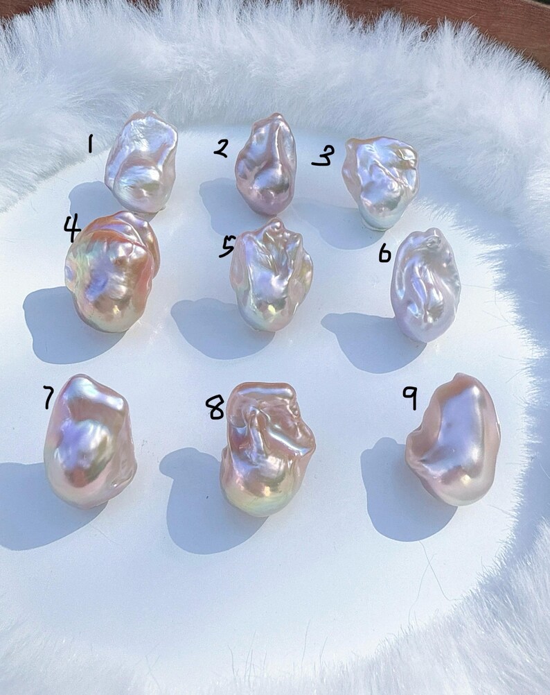 May include: Nine irregularly shaped, iridescent pearls are arranged on a white surface. The pearls display a range of colours, including pink, lavender, and gold, with a lustrous sheen. Each pearl is numbered from 1 to 9.