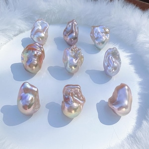 May include: Nine irregularly shaped baroque pearls with a shimmering, iridescent surface. The pearls exhibit a spectrum of colours, including pink, lavender, and gold, presented on a white surface. Each pearl has a unique form and size.
