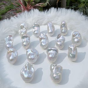 Puede incluir: Una colecci&oacute;n de perlas blancas brillantes de forma irregular. Las perlas est&aacute;n dispuestas sobre una superficie blanca con una textura suave y esponjosa. Las perlas tienen un brillo nacarado, que refleja la luz y crea una sutil iridiscencia. El tema general es el lujo y la belleza natural.