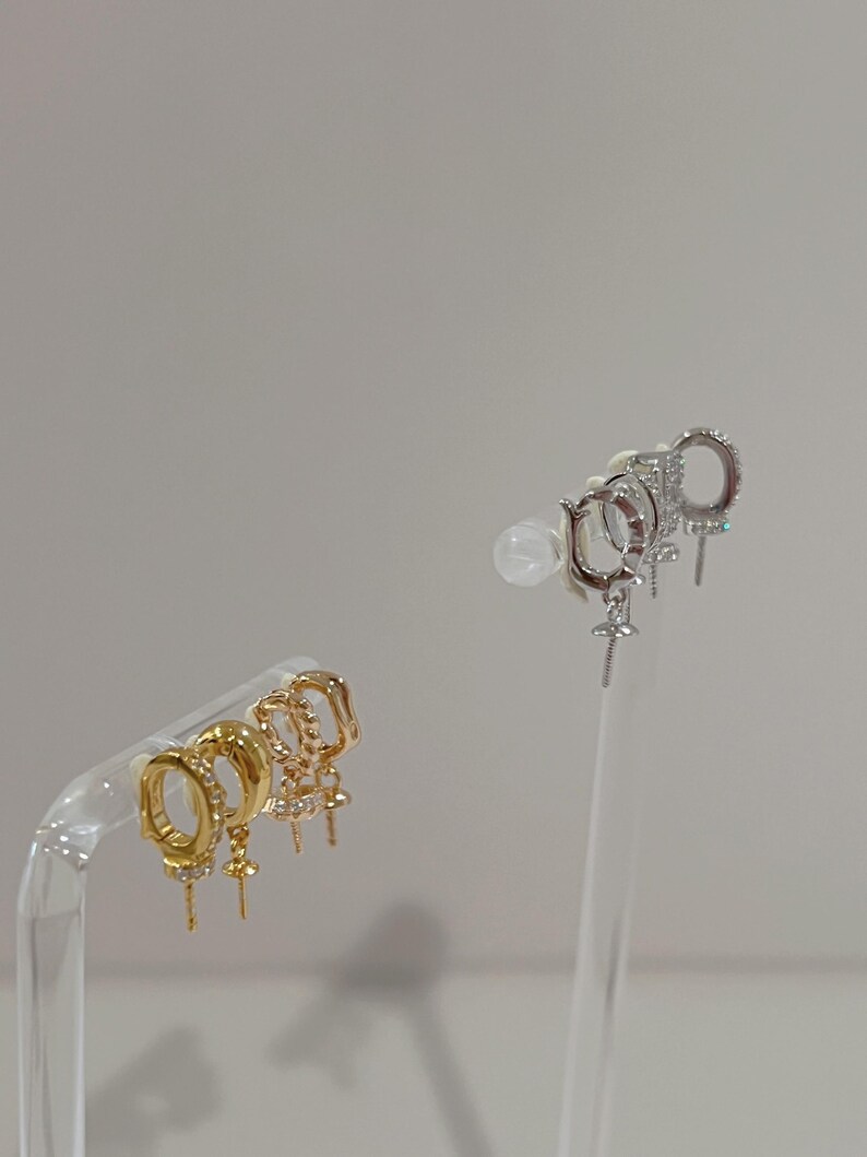 May include: A selection of gold and silver hoop earrings. The gold earrings feature different designs, some with small clear stones and hanging details. The silver earrings also have clear stones and a cross pendant. All earrings are displayed on clear stands.