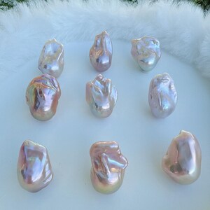 May include: Nine iridescent baroque pearls with a pearlescent sheen. The pearls display pink, gold, and silver hues, and are arranged on a white, fluffy surface. The pearls have irregular shapes, adding to their unique appeal. These are ideal for jewellery making.