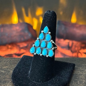 May include: A silver ring featuring a triangular arrangement of ten teardrop-shaped turquoise stones. Each stone is set in a smooth bezel with small silver bead accents between them, creating a cluster design that tapers to a point at the top.