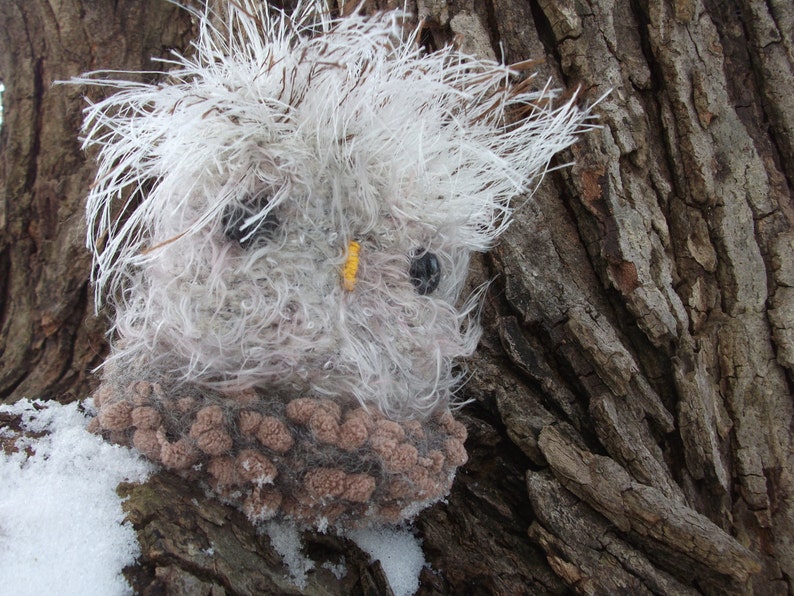 Pu&ograve; includere: Un giocattolo di peluche a forma di gufo, di colore bianco e marrone, con occhi neri e un becco giallo. Il giocattolo &egrave; seduto su un tronco d'albero.